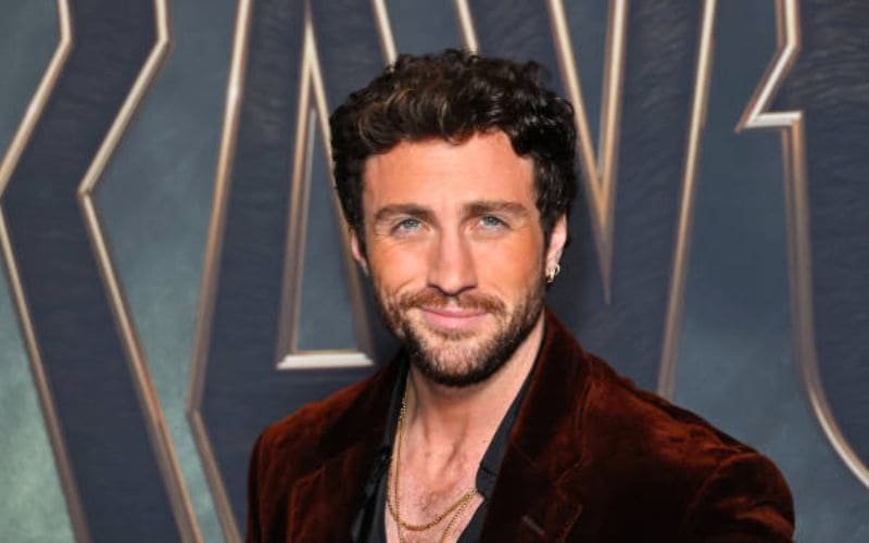 O ator Aaron Taylor-Johnson vestindo um blazer de veludo marrom, ilustrando sua trajetória completa de Kick-Ass até o papel de Kraven, O Caçador.
